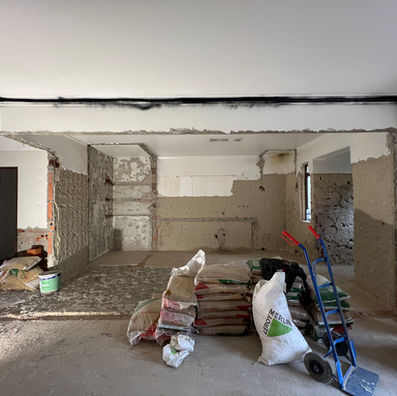 Apartamento em obras com abertura de parede, pavimento em cimento e elementos de construção.
