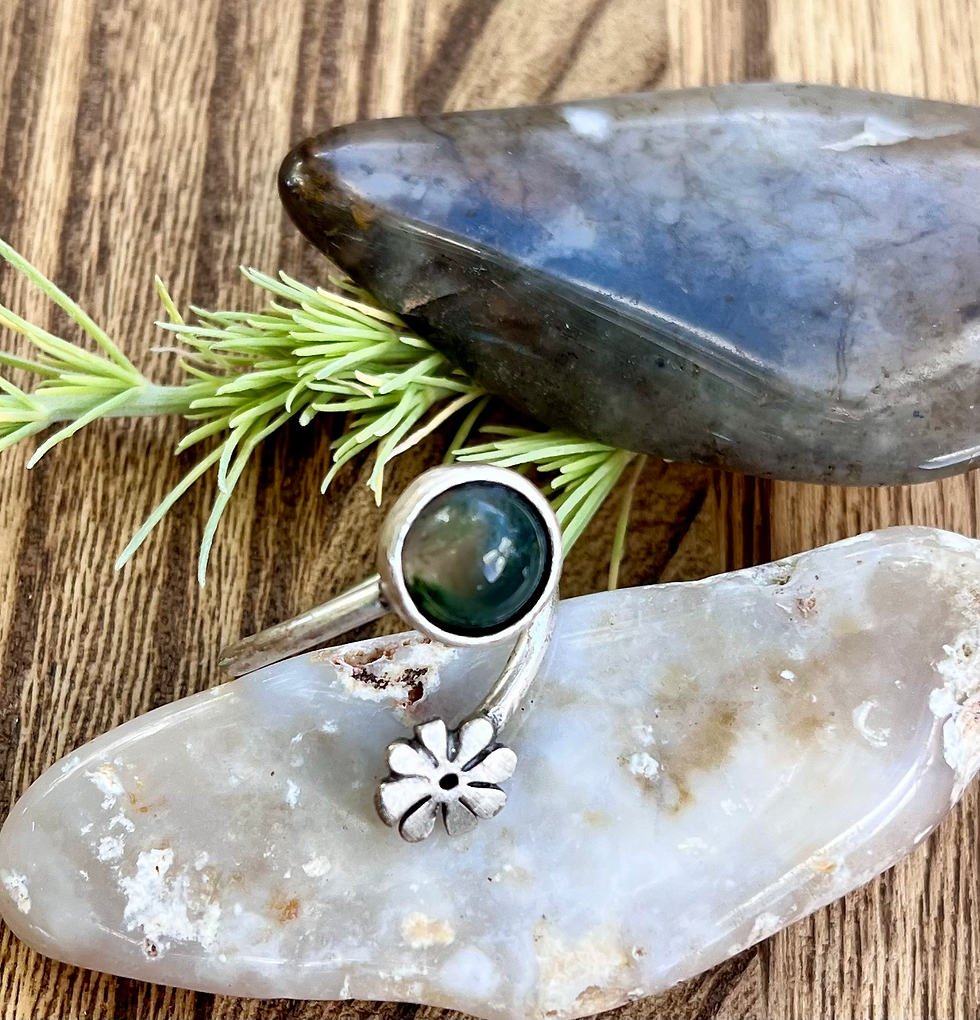 Miniatura: Silver ring with a green stone and flower detail on a stone surface.
