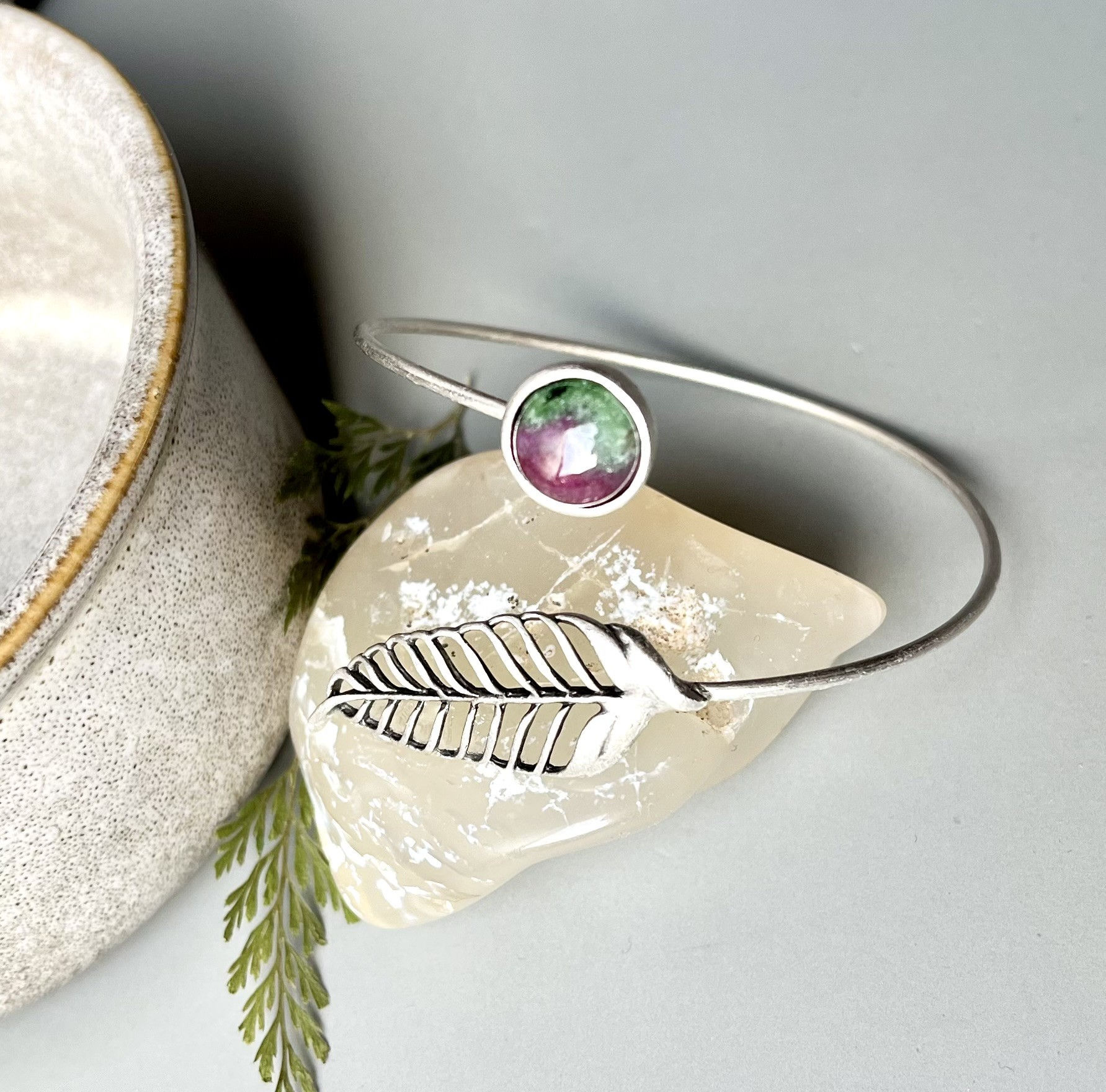 Silver cuff bracelet with a leaf and a ruby-colored gem setting.