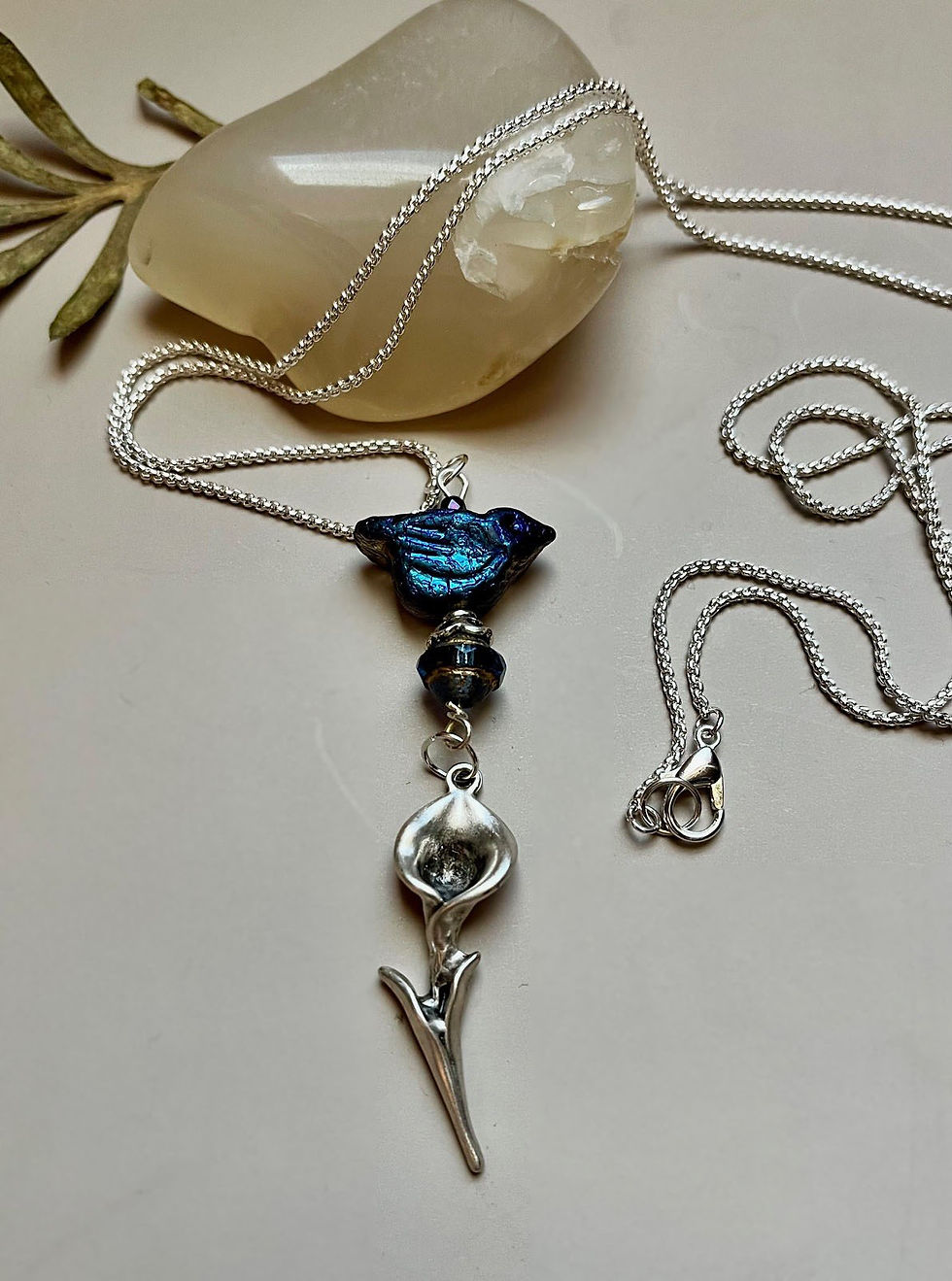 Miniature : Silver necklace with blue flower charm, beads, and white background.