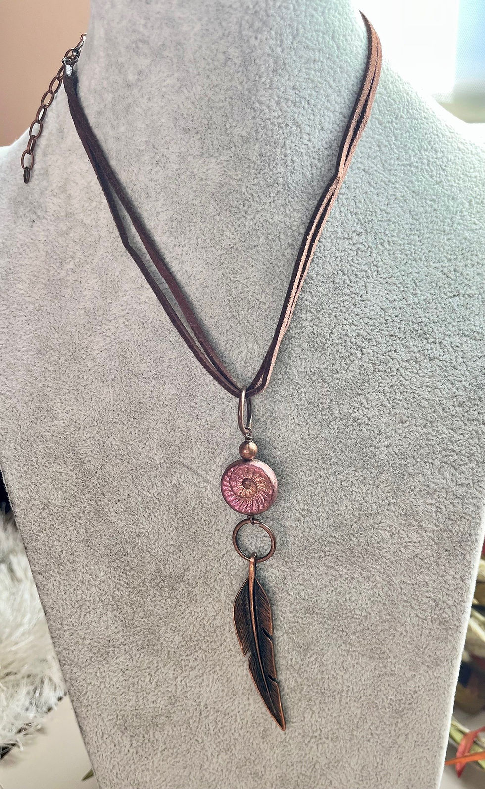 Miniatura: Copper necklace with pink stone pendant and feather on a gray background.