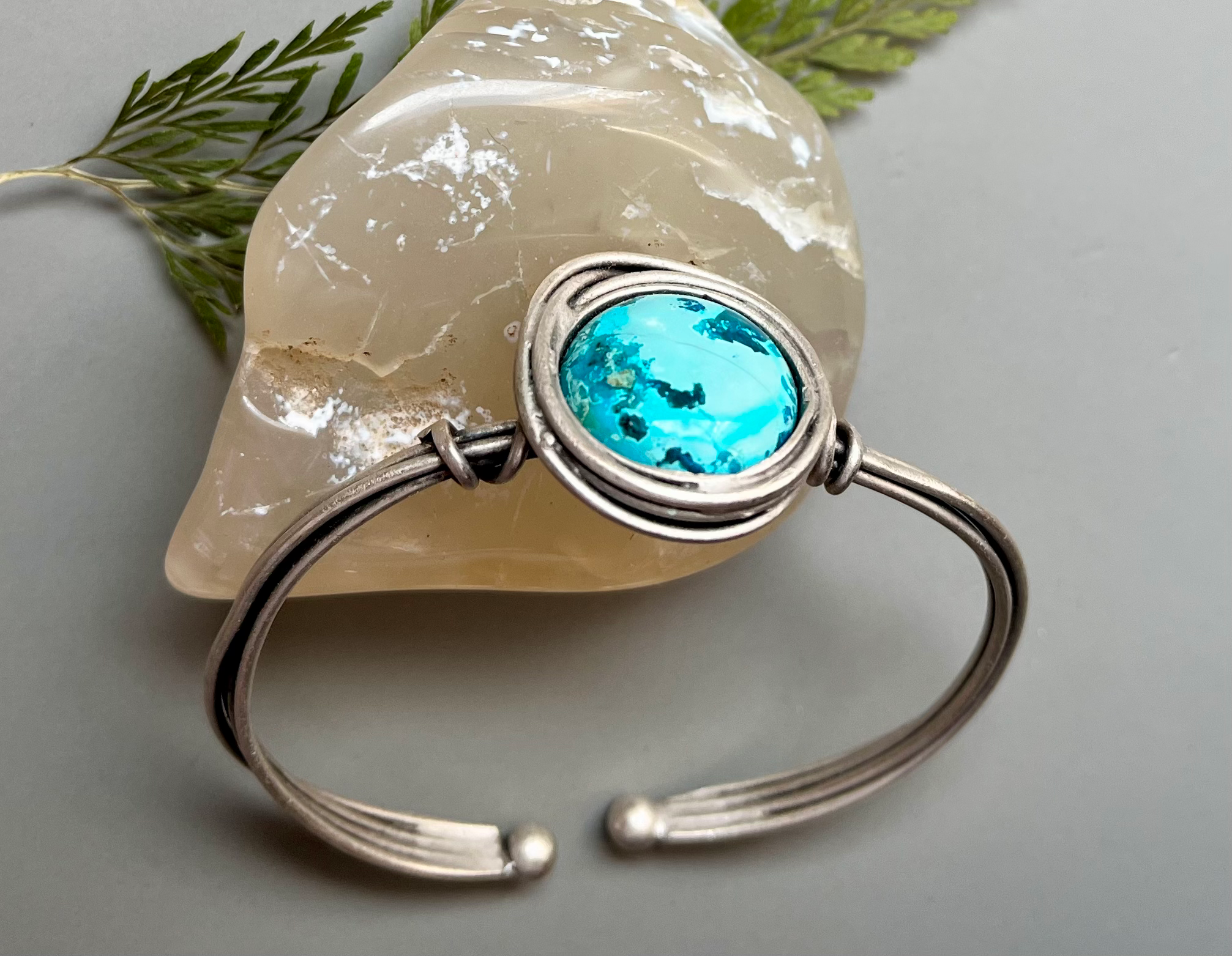 Silver cuff bracelet with turquoise stone, presented on a light gray surface.