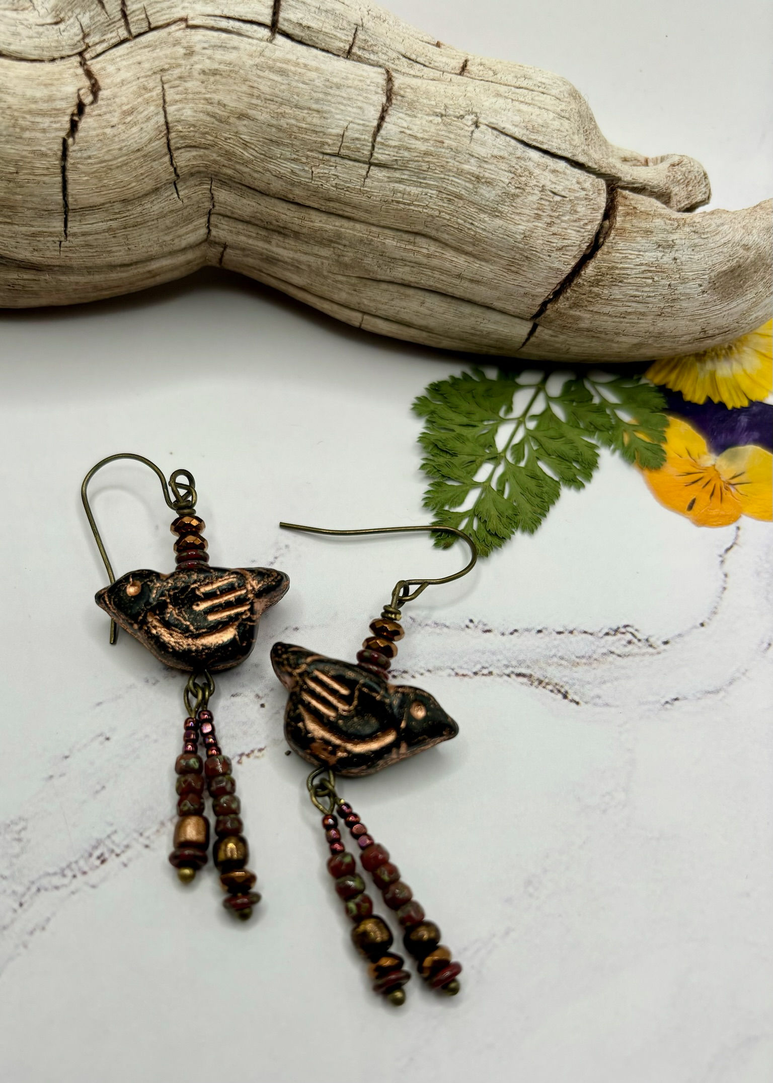 Copper bird earrings with beaded fringe and a wooden background, unique jewelry.