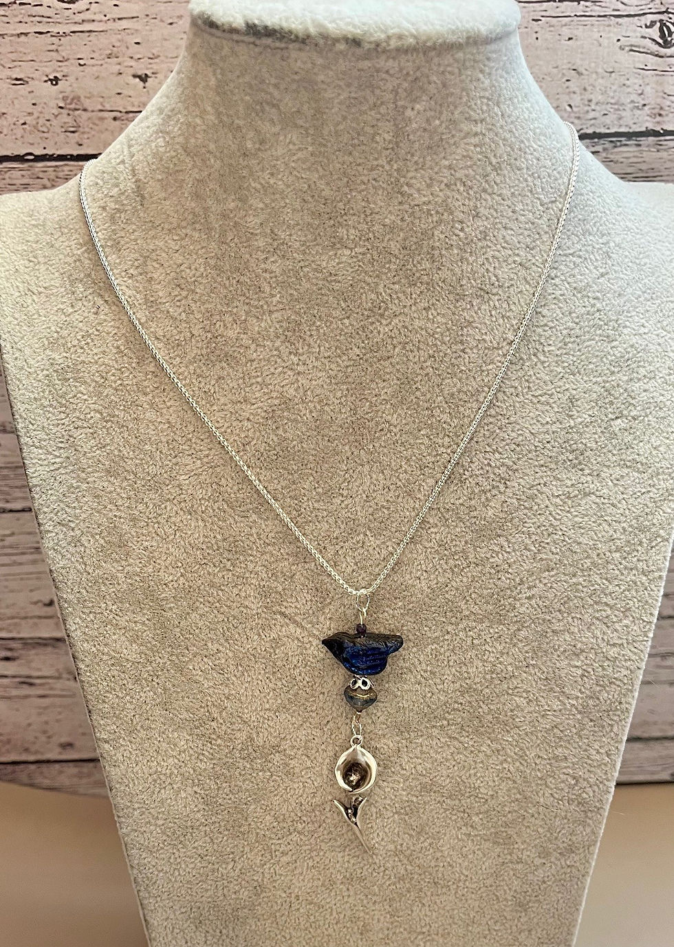 Miniature : Silver necklace, blue pendant, and small charms displayed on a bust backdrop