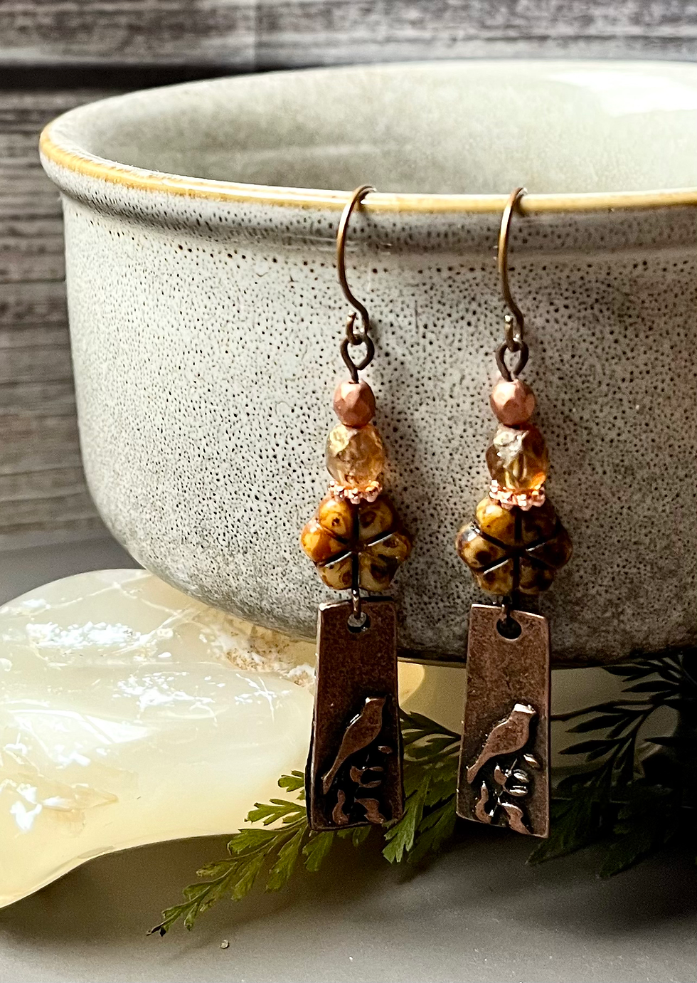 Copper earrings with bird details, flower beads, and a neutral background.