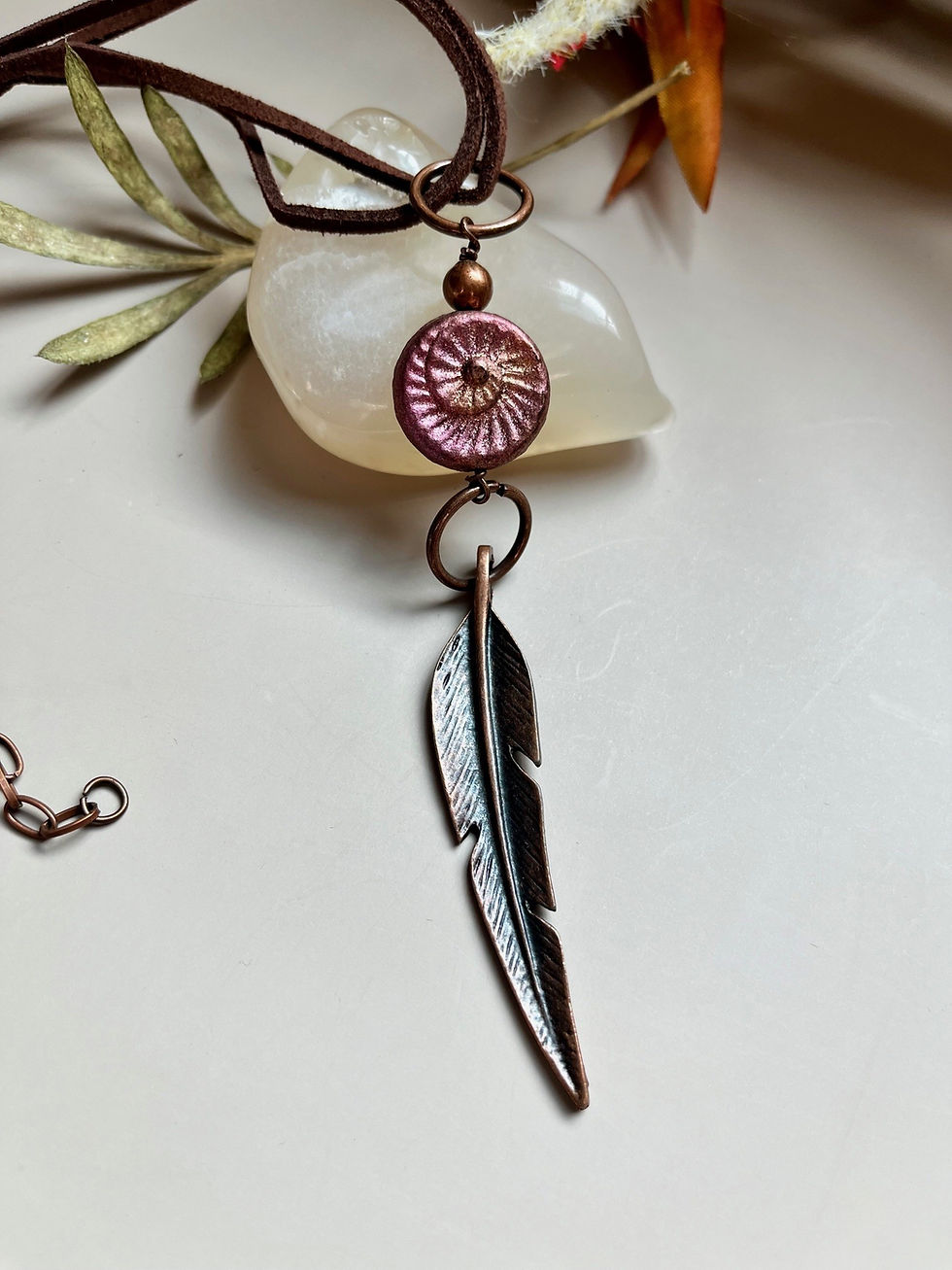 Copper feather pendant necklace with a pink bead and decorative background