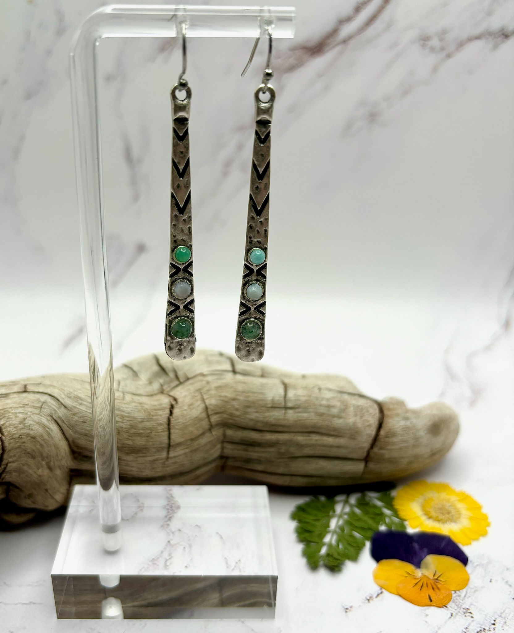Silver earrings with turquoise and white stones, displayed on a wooden stand.