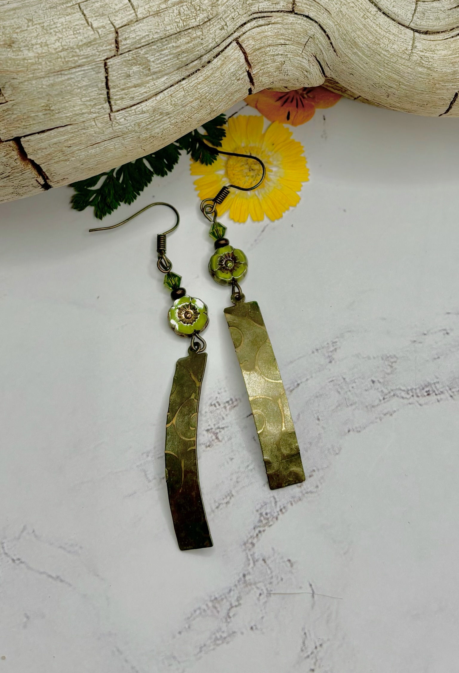 Handmade earrings with brass bars and green beads hanging on display