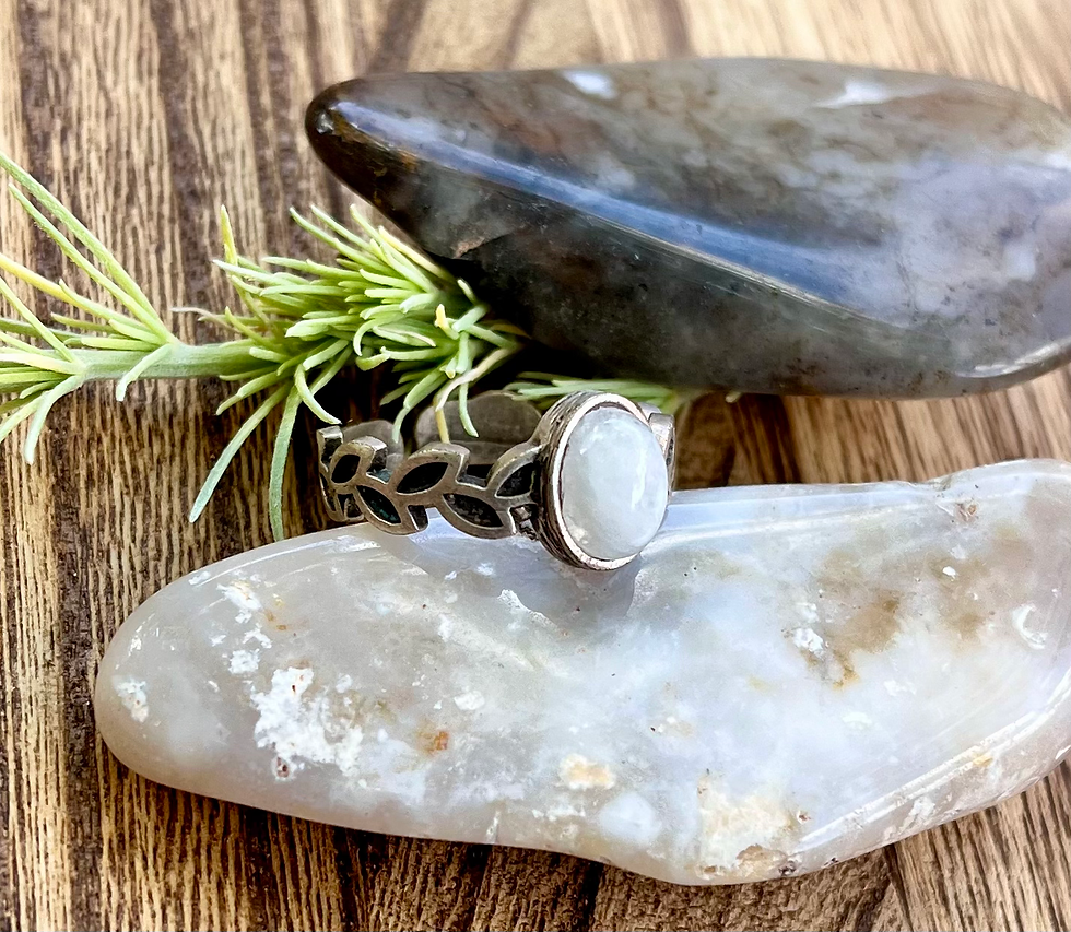 Miniatura: Silver ring with white stone, leaves, and organic shapes on a stone backdrop.