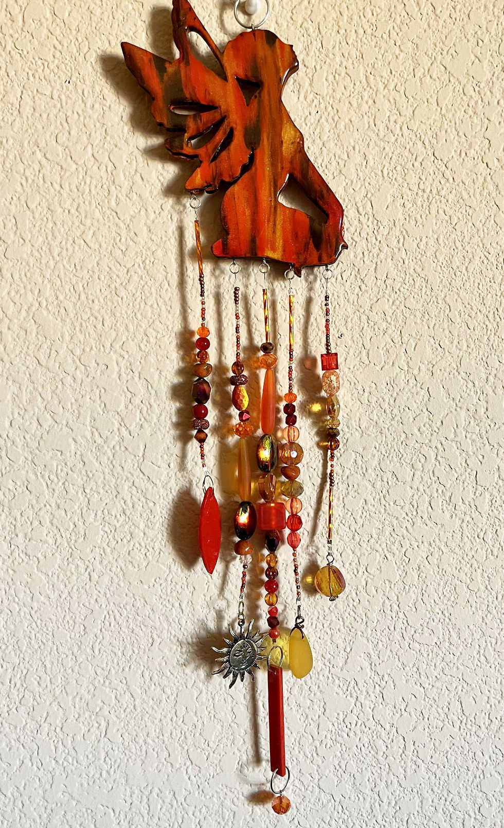 Miniature : Orange elephant wind chime, beads, and hanging ornaments displayed on a wall.