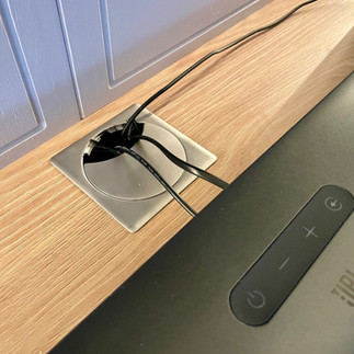 Bespoke made-to-measure media wall with integrated storage, open shelving, ambient LED lighting and discreet sockets in a modern open-plan lounge.