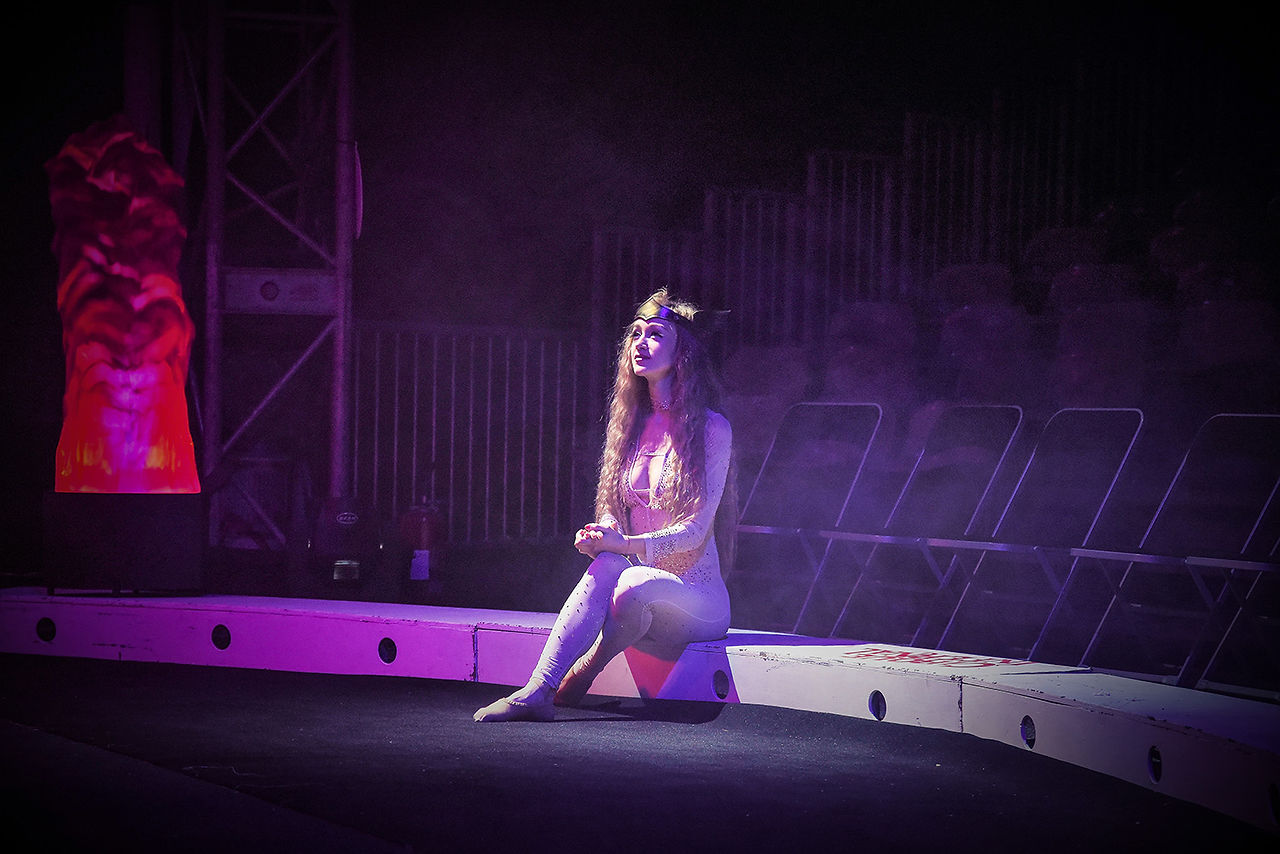 Artiste assise sur la scène du Cirque Infernal sous des lumières violettes.