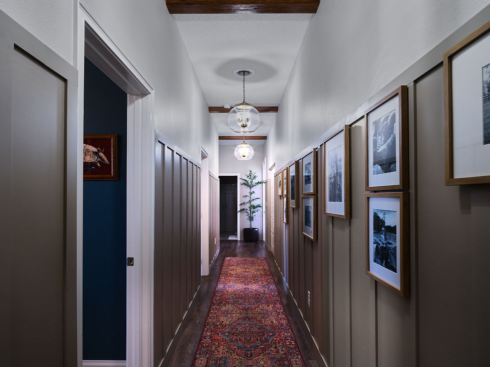 Emerald Oaks Farm hallway with painted wainscoting, framed photographs, ceiling beams and a patterned runner.
