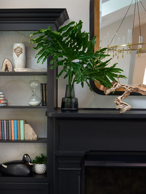 Black fireplace mantel styled with greenery beside shelves of books and decorative objects