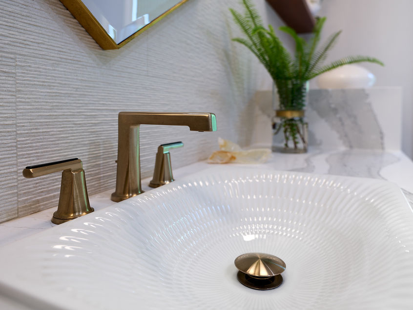 Textured white bathroom basin with an angular brass faucet and matching handles