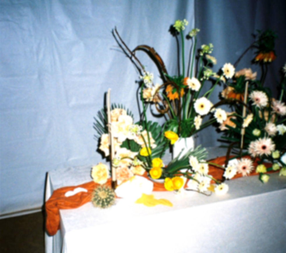 Floral arrangements with white, yellow, and orange flowers on a draped table against a blue backdrop.