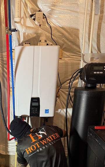 Hot Water Pros technician working on a wall-mounted tankless water heater next to a water softener