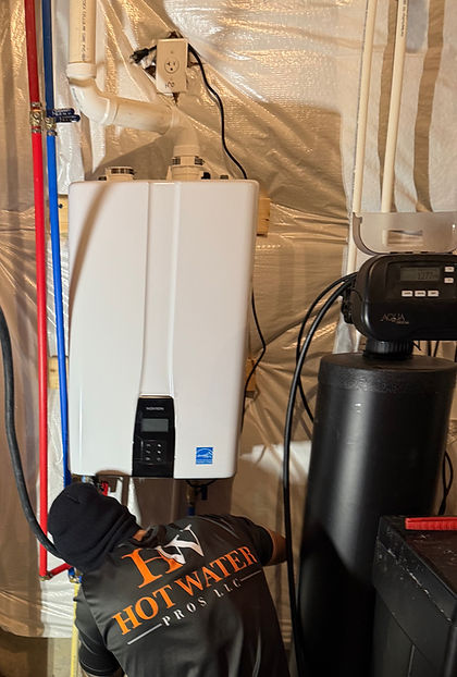 Hot Water Pros technician working on a wall-mounted tankless water heater next to a water softener