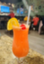 A colorful Hurricane cocktail topped with a cherry and orange slice sits on a table with the bar in the background at Bourbon Street Bistro in Charleston, WV