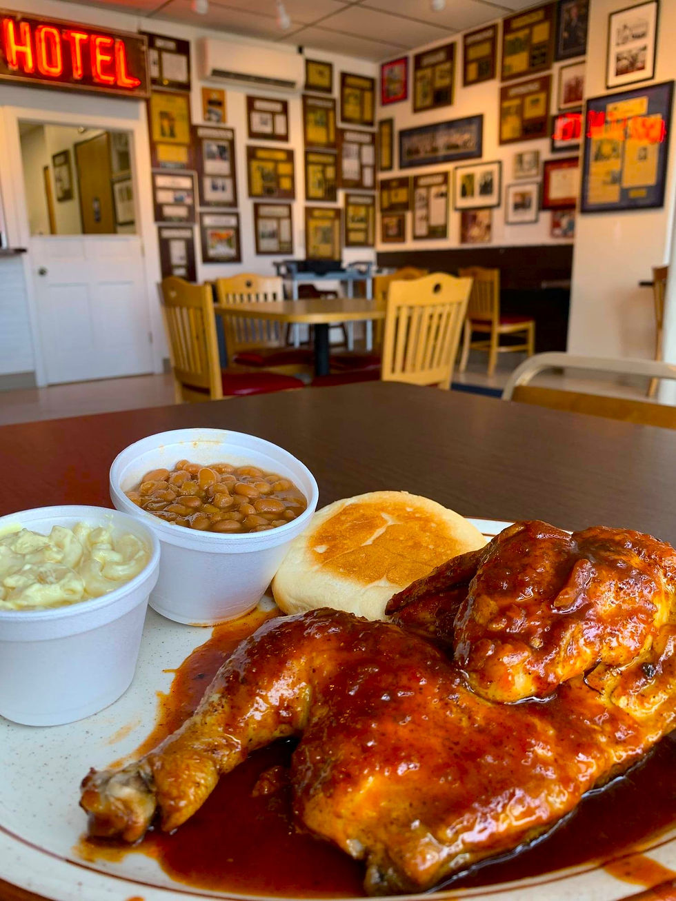 A platter of BBQ chicken and side dishes sits on a table inside a restaurant
