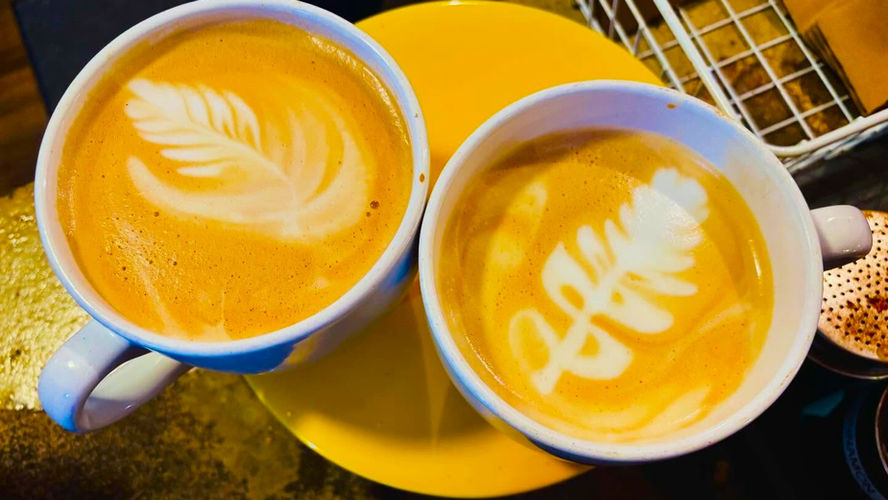 Two cups of coffee with elaborate foam art sit on a table inside a coffee shop