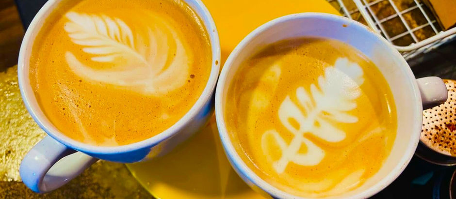 Two cups of coffee with elaborate foam art sit on a table inside a coffee shop