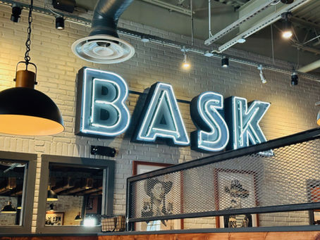 A neon light of the name BASK is displayed inside a restaurant dining room