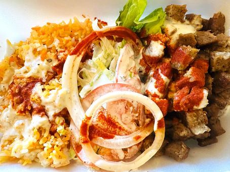 A halal lamb platter featuring sliced lamb, rice, tomatoes, lettuce and onion topped with red and white sauces