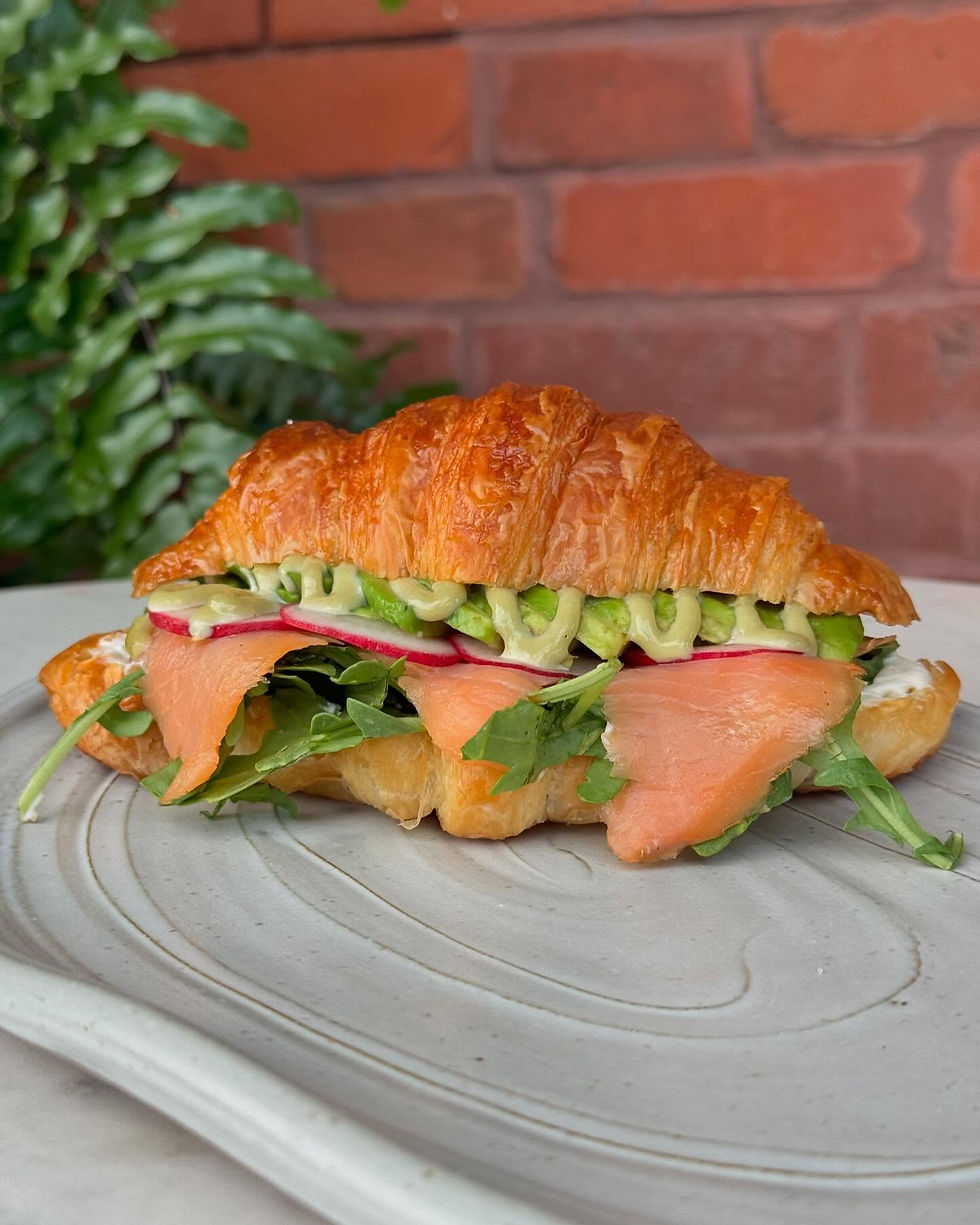 A smoked salmon sandwich on a fresh croissant with fresh veggies and sauce