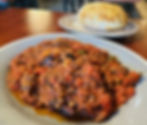 A large plate is filled with a mixture of eggplant, tomatoes, ground beef, peppers and more with a giant mound of puffed bread in the background at Milano's Italian Restaurant in Charleston, WV