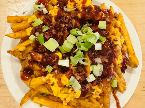 A plate of fries covered with pimento cheese, BBQ sauce and scallions