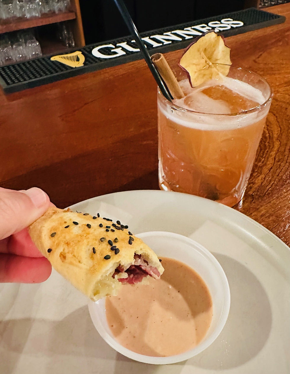 A mini Reuben pie and a plum cocktail sit atop a bar in an Irish pub