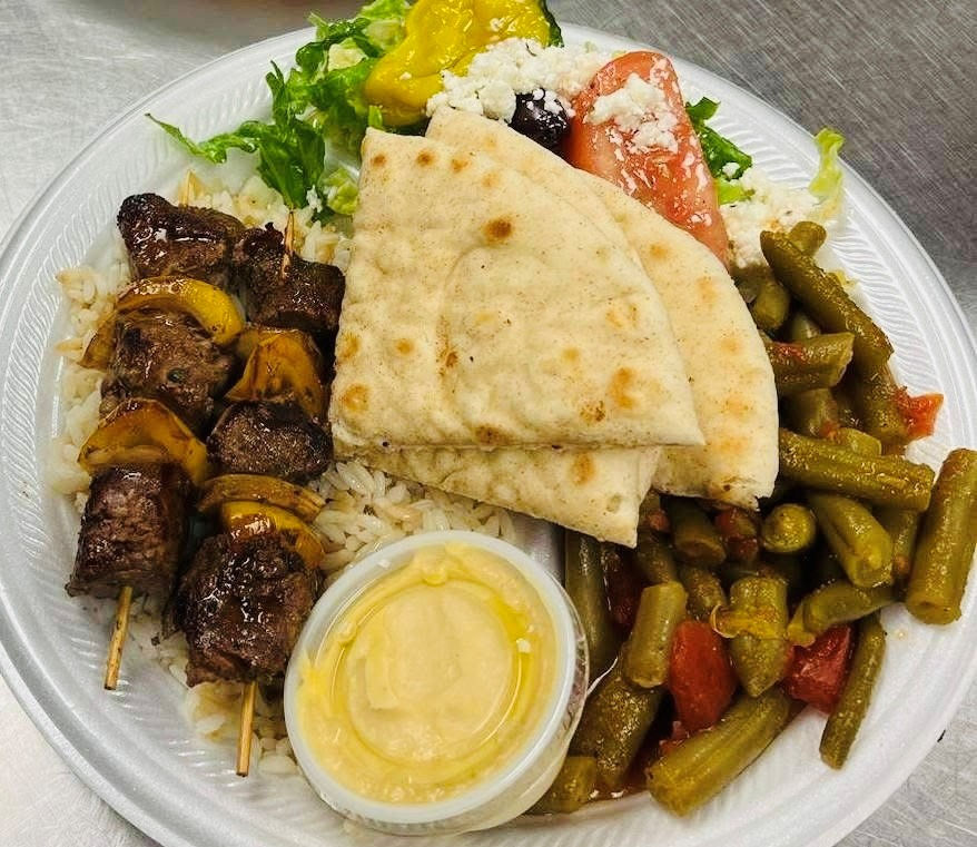 A plate of beef kebabs, rice, green beans, Greek salad, hummus and pita