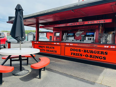 Tables in front of a bright orange old-fashioned hot dog drive-in