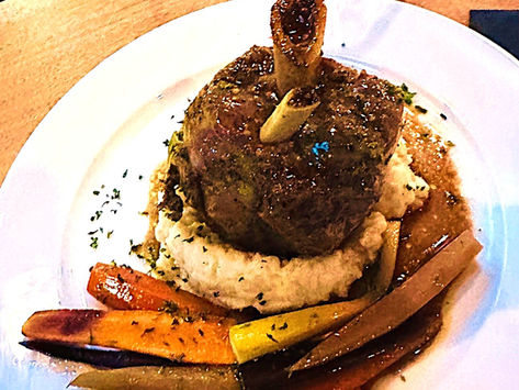 A large glistening pork shank atop a mound of mashed potatoes and colorful carrots
