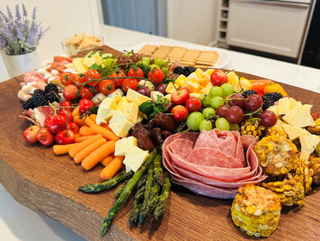 A large antipasti board is piled with fresh meats, cheeses, vegetables, fruits and more