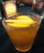 A bourbon cocktail with sliced of peach sitting on a table