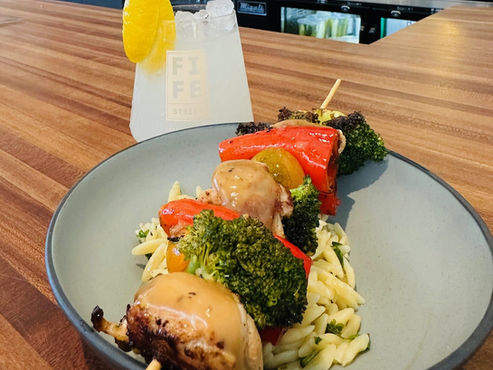 Mediterranean chicken and veggie kabobs atop rice, paired with a lemon spritz cocktail sitting on a bar