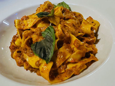 A bowl of wide noodle pasta glistening with meat sauce and fresh herbs