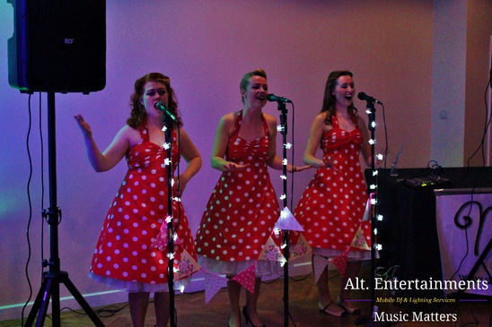 Wedding singers performing live at a reception at Fordhouses Cricket Club in Wolverhampton. The image shows the singers engaging with the audience on stage, with professional sound equipment and elegant lighting in the background. The setting is beautifully decorated, reflecting the sophisticated atmosphere created by Alt. Entertainments. Guests are seen enjoying the lively performance, adding to the festive mood of the event.