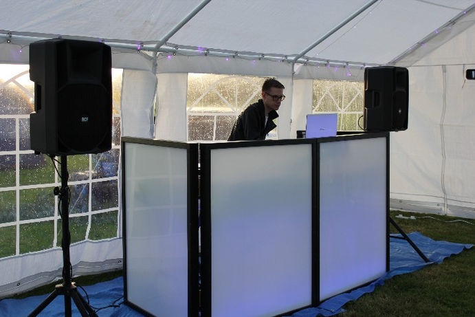 Photograph of a professional mobile DJ setup at a festival in Northamptonshire/Rutland, featuring advanced sound systems and LED lighting. The image, taken by Alt. Entertainments, showcases the expertly arranged DJ booth designed to create an electrifying atmosphere at the event.