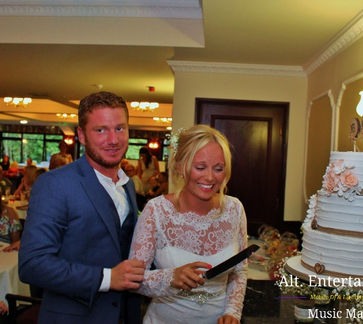 Newly married couple joyfully cutting their wedding cake surrounded by guests at Beau Desert Golf Club in Cannock, Staffordshire, symbolizing the start of their marital journey.