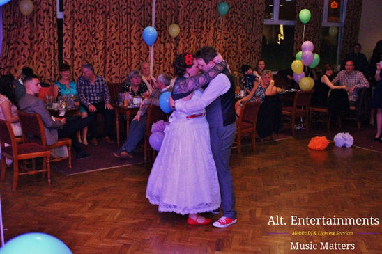 Bride and groom dancing together for their first dance at a wedding disco at Fordhouses Cricket Club in Wolverhampton. The couple is surrounded by soft, ambient lighting, adding a romantic glow to the scene. The DJ setup by Alt. Entertainments is visible in the background, contributing to the special atmosphere of the evening.