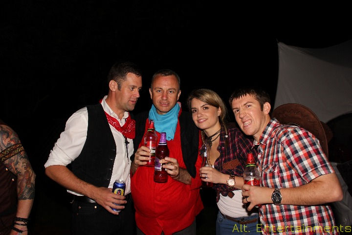 A diverse group of elegantly dressed guests joyfully posing for a photo outdoors in Warwickshire, captured by Alt. Entertainments Mobile DJ, Disco & Events company. The image captures a moment of celebration and camaraderie amidst the natural beauty of Warwickshire's countryside, illuminated by soft natural light.