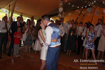 The bride and groom share their first dance at Market Overton, Oakham, Rutland, captured by Alt. Entertainments. The photo shows the couple in a tender moment, with the bride in a white gown and the groom in a classic suit, dancing under soft ambient lighting. The DJ setup in the background reflects Alt. Entertainments' role in creating a memorable wedding atmosphere. The image highlights the elegance and romance of the first dance, set against a beautifully decorated venue.