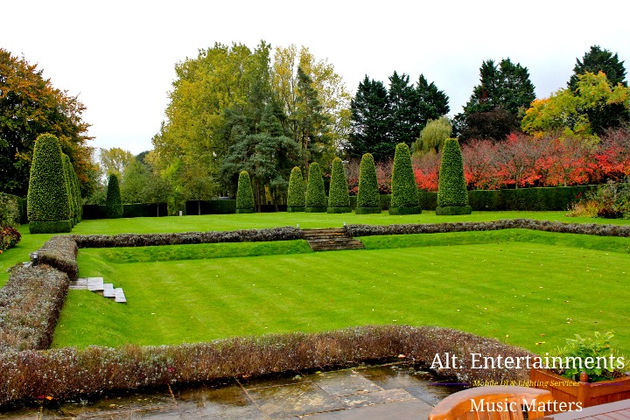 A picturesque view of the Astley Manor House Gardens in Stow-on-the-Wold, Gloucestershire/Cotswolds, captured by Alt. Entertainments, showcasing the lush greenery, vibrant flower beds, and serene ambiance of the tranquil garden retreat.