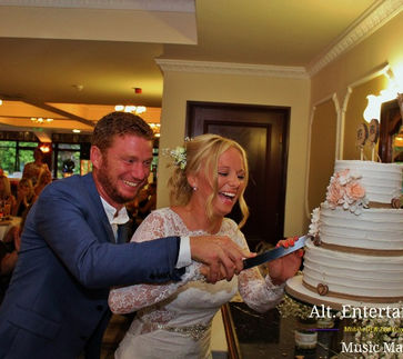 Newlyweds cutting their wedding cake at Beau Desert Golf Club in Cannock, Staffordshire, surrounded by family and friends, marking the start of their marital bliss.