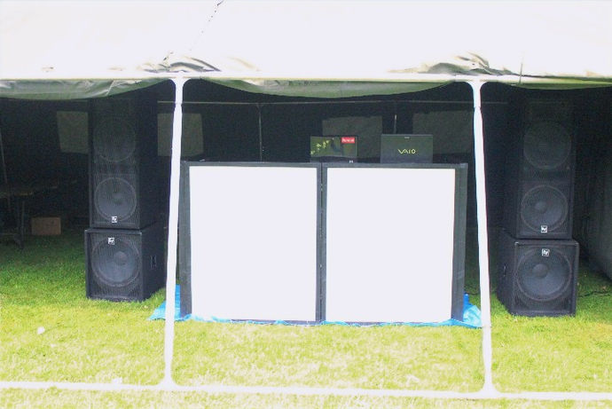 A vibrant mobile DJ setup at a Warwickshire festival, featuring large speakers, colorful lighting, and a well-equipped DJ booth. Festival-goers dance and enjoy the music, creating an energetic and lively atmosphere. The setup, provided by Alt. Entertainments, highlights their expertise in delivering unforgettable event entertainment.