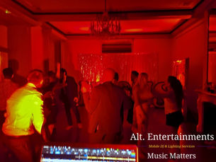 Guests dancing joyfully at a wedding disco in Garthmyl Hall, Montgomery, Wales. The photo, taken by Alt. Entertainments, shows a vibrant dance floor filled with happy guests moving to the music, illuminated by warm, inviting lighting within the elegant setting of the historic Garthmyl Hall.