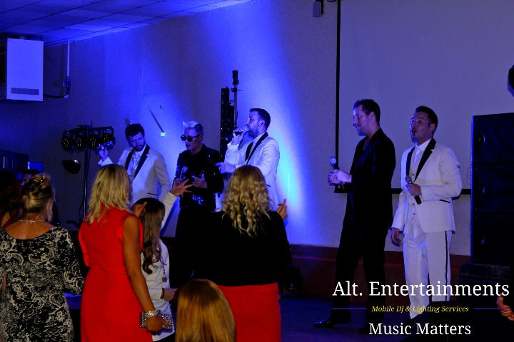 The Jersey Boys performing on stage at Wolverhampton Racecourse, bathed in vibrant lighting, with an enthusiastic crowd enjoying the music, captured by Alt. Entertainments, a mobile DJ, disco, and events company.